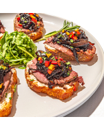Mini Filet Crostini. Close-up view of crostini topped with beef, caramelized onion, and bell pepper, on a plate