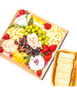 A close-up top view of a cheese tray with brie, grapes, strawberries, and wine cheese spread