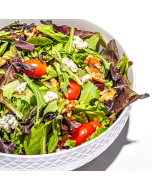Close-up view of spring mix salad on a white plate, topped with walnuts, crumbly cheese, and cherry tomatoes