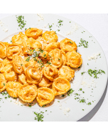 Oblique close-up of tortellini is a rose sauce served in a square white ceramic bowl