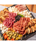 Overhead view of a charcuterie board. Salamis, prosciutto, cheese, crostini, and olives, arranged for serving on a black tray 