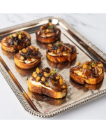 Oblique shot of crostini topped with brie, bacon, and apple jam; served on a silver platter.