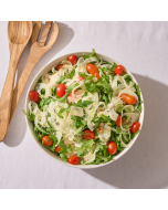 Close-up view of spring mix salad on a white plate, topped with walnuts, crumbly cheese, and cherry tomatoes