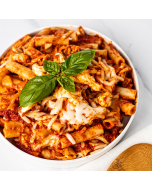 Overhead closeup of baked ziti served in a white ceramic bowl, garnished with a sprig of basil
