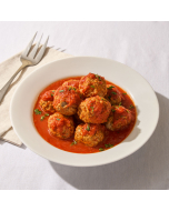 Oblique view of large meatballs in red sauce in a speckled, white, stoneware dish