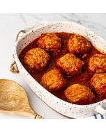 Oblique view of large meatballs in red sauce in a speckled, white, stoneware dish