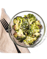 Close up view of roasted broccoli topped with asiago cheese, served in a white stoneware bowl