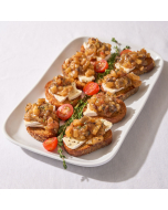 Oblique shot of crostini topped with brie, bacon, and apple jam; served on a silver platter.