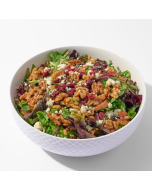 Close-up view of spring mix salad on a white plate, topped with walnuts, crumbly cheese, and cherry tomatoes