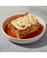 Side view of eggplant parmigiano garnished with a sprig of basil and served on a white plate