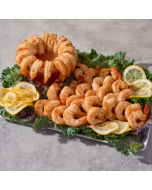 Oblique overhead view of seasoned shrimp arranged for shrimp cocktail around cocktail sauce, on a bed of lettuce with lemon wedges