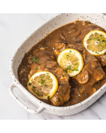 Oblique overhead view of chicken marsala, topped with rounds of lemon, served in a white stoneware dish