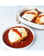 Oblique view of chicken parmigiano served in a white bowl, with a casserole dish of chicken parmigiano in the background