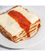 Side view of eggplant parmigiano garnished with a sprig of basil and served on a white plate
