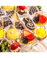 Overhead view of miniature pastries arranged in rows on a table cloth, including raspberry tulip cups, lemon cream baskets, miniature seasonal fruit tarts, miniature chocolate éclairs, and Passion fruit glazed cream puffs
