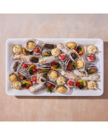 Overhead view of miniature pastries arranged in rows on a table cloth, including raspberry tulip cups, lemon cream baskets, miniature seasonal fruit tarts, miniature chocolate éclairs, and Passion fruit glazed cream puffs