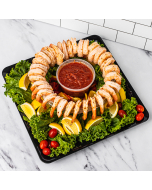 Oblique overhead view of seasoned shrimp arranged for shrimp cocktail around cocktail sauce, on a bed of lettuce with lemon wedges