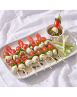 Overhead view of caprese skewers: Mozzarella, grape tomato, and basil on a skewer on a wooden board