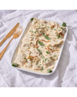 Overhead view of ravioli tossed in a mushroom cream sauce, served in a square dish.