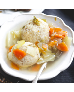 Overhead view of matzo ball soup served in a white scalloped bowl