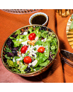 Close-up view of spring mix salad on a white plate, topped with walnuts, crumbly cheese, and cherry tomatoes