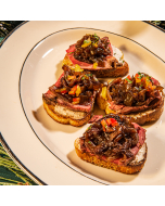 Mini Filet Crostini. Close-up view of crostini topped with beef, caramelized onion, and bell pepper, on a plate