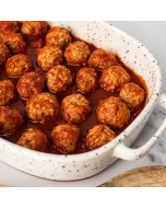 Overhead closeup of miniature meatballs in red sauce served in a speckled, white, stoneware casserole dish