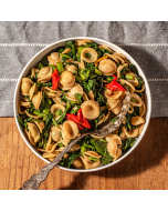 Close-up of orrechiette pasta with sliced sausage, broccoli rabe, and red and yellow peppers, served in a white bowl