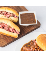 Two football rolls filled with rare-roasted beef served on a wooden platter with a side of au jus