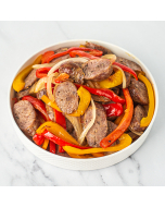 Closeup of sliced sausage, peppers, and onions, served in a white bowl.