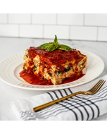 Oblique view of a piece of spinach and cheese lasagna served on a white ceramic plate and garnished with basil