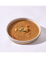 Oblique photo of Vegetarian Lentil Soup in a white bowl with a tomato in the background