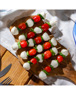 Overhead view of caprese skewers: Mozzarella, grape tomato, and basil on a skewer on a wooden board
