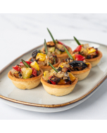 Oblique shot of small pastry tarts filled with ratatouille and garnished with rosemary.