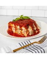 Side view of vegetable lasagna covered in red sauce, garnished with a sprig of basil, and served on a white ceramic plate.