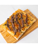 Overhead view of a corner piece of anchovy and herb-topped focaccia bread, served on a bamboo platter