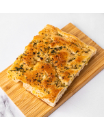 Overhead view of a corner piece of herb-topped focaccia bread, served on a bamboo platter