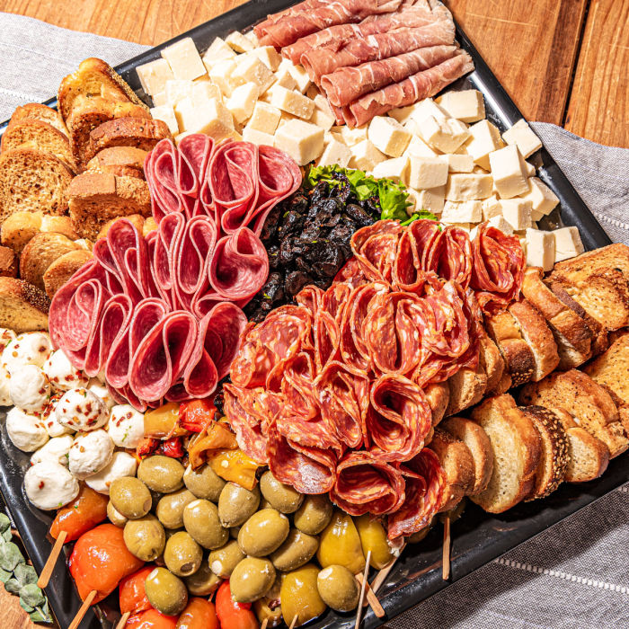 Overhead view of a charcuterie board. Salamis, prosciutto, cheese, crostini, and olives, arranged for serving on a black tray 