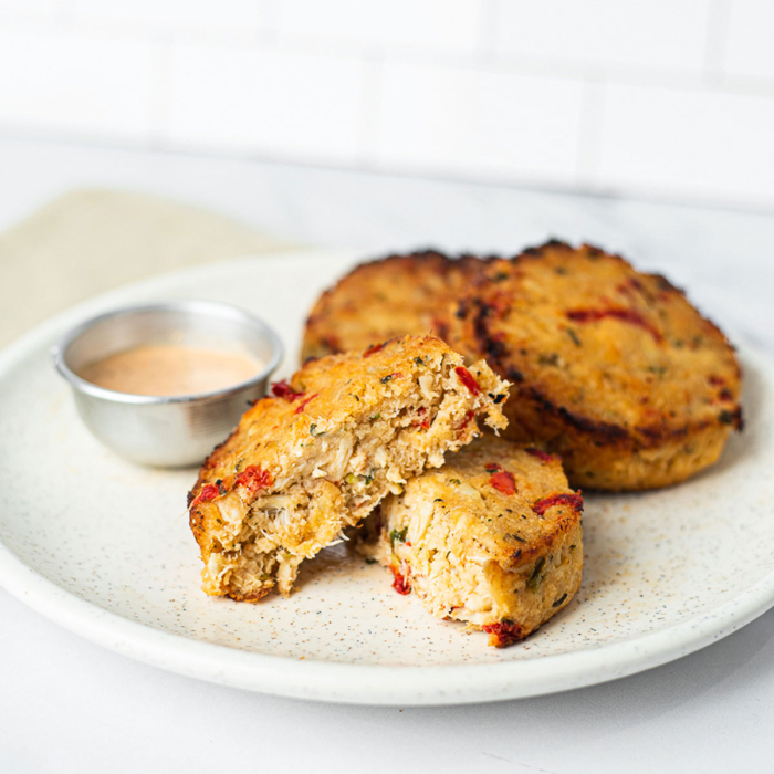 Oblique view of crabcakes served on a white stoneware plate, with a side of spicy tartar sauce