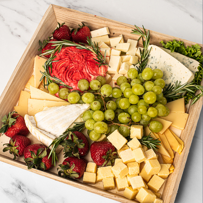 A close-up top view of a cheese tray with brie, grapes, strawberries, and wine cheese spread
