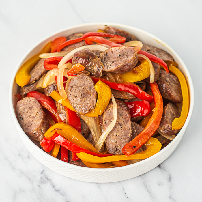 Closeup of sliced sausage, peppers, and onions, served in a white bowl.