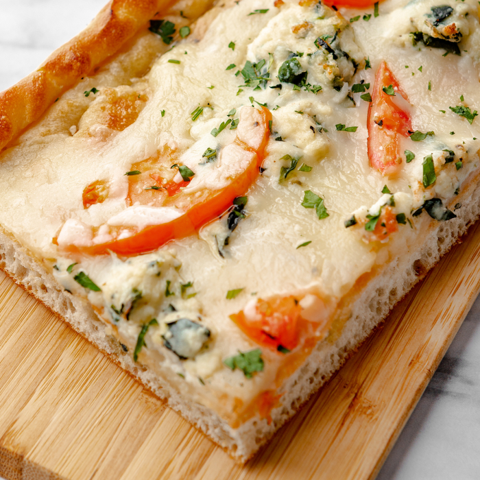 Close-up overhead view of an edge piece of square white pizza topped with sliced tomatoes, spinach, and ricotta cheese