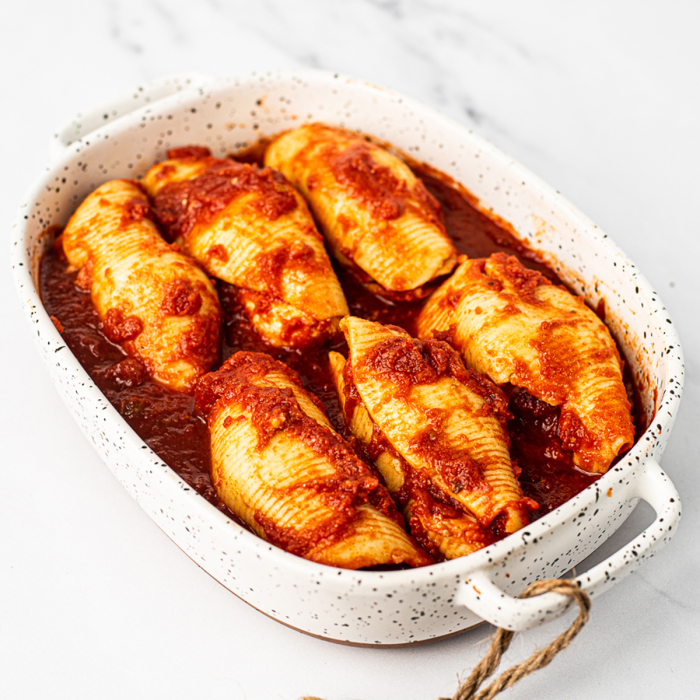 Six stuffed shells in red sauce, served in a white speckled stoneware casserole dish
