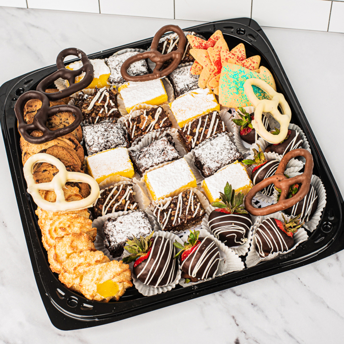 Overhead view of various sweets arranged in a black plastic serving tray.  Including chocolate covered pretzels, miniature brownies, miniature lemon bars, chocolate covered strawberries, and sugar cookies