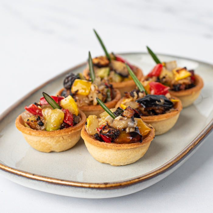 Oblique shot of small pastry tarts filled with ratatouille and garnished with rosemary.