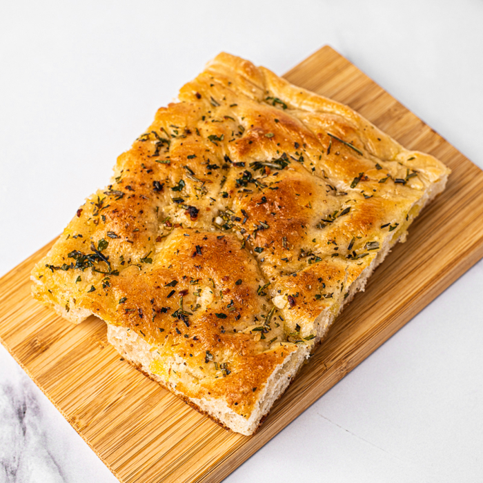 Overhead view of a corner piece of herb-topped focaccia bread, served on a bamboo platter